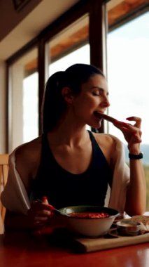 Genç bir kadın, pencereden dağları gören bir restoranda ekmekle pancar çorbası yiyor. Ukrayna mutfağı konsepti. Kırmızı borş çorbası. Dikey video