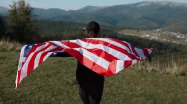 Genç bir kadın bir Amerikan bayrağını dağın tepesinde tutuyor. Amerikan bayrağı taşıyan bir kadın. Özgürlük ve demokrasi kavramı. ABD 'de seçimler