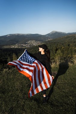 Genç bir kadın bir Amerikan bayrağını dağın tepesinde tutuyor. Amerikan bayrağı taşıyan bir kadın. Özgürlük ve demokrasi kavramı. ABD 'de seçimler