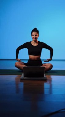 Bilgisayarla yoga yapan genç bir kadın..