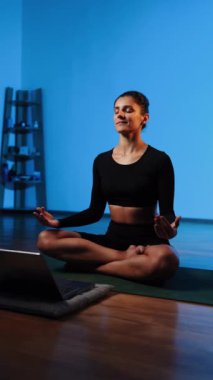 Bilgisayarla yoga yapan genç bir kadın..