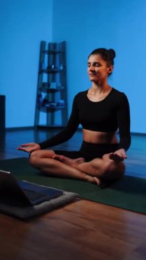 Bilgisayarla yoga yapan genç bir kadın..