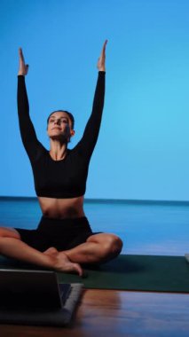 Bilgisayarla yoga yapan genç bir kadın..