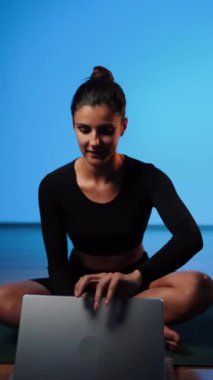 Bilgisayarla yoga yapan genç bir kadın..