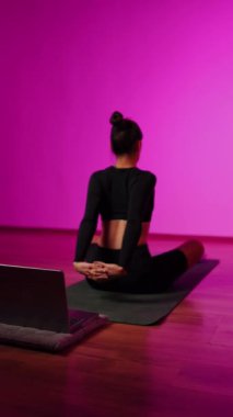 Bilgisayarla yoga yapan genç bir kadın..