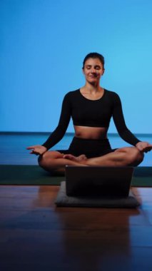 Bilgisayarla yoga yapan genç bir kadın..