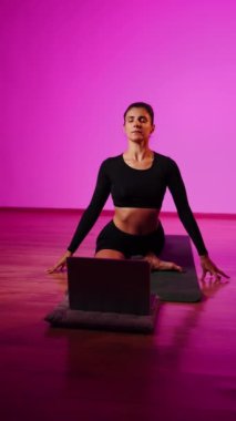 Bilgisayarla yoga yapan genç bir kadın..