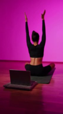 Bilgisayarla yoga yapan genç bir kadın..