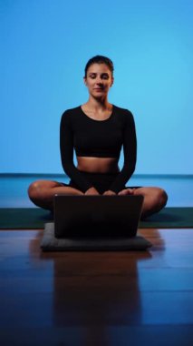 Bilgisayarla yoga yapan genç bir kadın..