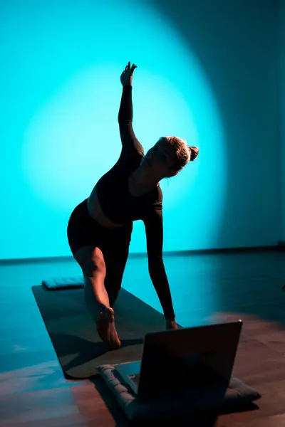 stock image Young woman doing yoga online with laptop.Woman meditating in studio in neon light with laptop.Concept of yoga and meditation online.Vertical photo