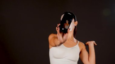 Genç bir kadın koyu bir arka plana kozmetik maske takıyor. Ev yapımı yüz bakımı konsepti. Yüz bakımı için kozmetik maske 4k