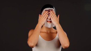 Genç bir kadın koyu bir arka plana kozmetik maske takıyor. Ev yapımı yüz bakımı konsepti. Yüz bakımı için kozmetik maske 4k