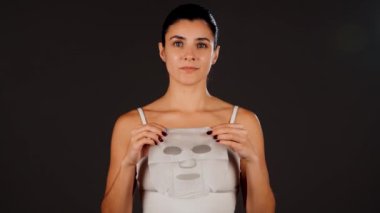 Genç bir kadın koyu bir arka plana kozmetik maske takıyor. Ev yapımı yüz bakımı konsepti. Yüz bakımı için kozmetik maske 4k