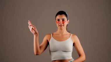 Mükemmel parıldayan derisi ve kameraya poz veren doğal makyajlı genç bir kadın. Gözlerinin altında yorgunluk ve şişkinliği azaltmak için kolajen bantları var. Deri bakımı. Modern güzellik aletleri konsepti 4k.