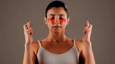 Mükemmel parıldayan derisi ve kameraya poz veren doğal makyajlı genç bir kadın. Gözlerinin altında yorgunluk ve şişkinliği azaltmak için kolajen bantları var. Deri bakımı. Modern güzellik aletleri konsepti 4k.