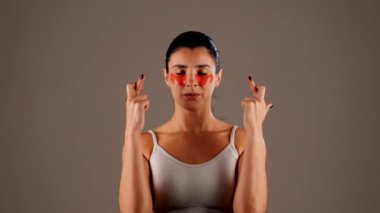 Mükemmel parıldayan derisi ve kameraya poz veren doğal makyajlı genç bir kadın. Gözlerinin altında yorgunluk ve şişkinliği azaltmak için kolajen bantları var. Deri bakımı. Modern güzellik aletleri konsepti 4k.