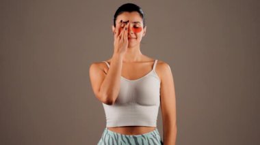 Mükemmel parıldayan derisi ve kameraya poz veren doğal makyajlı genç bir kadın. Gözlerinin altında yorgunluk ve şişkinliği azaltmak için kolajen bantları var. Deri bakımı. Modern güzellik aletleri konsepti 4k.