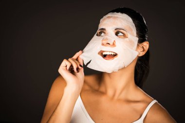 Genç bir kadın koyu bir arka plana kozmetik maske takıyor. Ev yapımı yüz bakımı konsepti. Yüz bakımı için kozmetik maske 4k