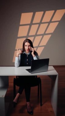 Dizüstü bilgisayarla çalışan bir kadın telefonda konuşuyor. Bir destek işçisinin portresi. Uzaktan çalışma konsepti. Dikey video
