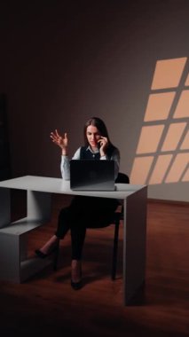 Dizüstü bilgisayarla çalışan bir kadın telefonda konuşuyor. Bir destek işçisinin portresi. Uzaktan çalışma konsepti. Dikey video