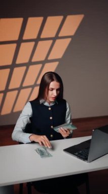 Bir kadın finansör dizüstü bilgisayarda çalışırken kârı sayar. Bir kadın para sayar. İş konsepti. Dikey video