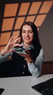 Genç bir kadın dizüstü bilgisayarın başında otururken para fırlatıyor. Bu kadın çok para kazandı. Finansal başarı kavramı. Dikey video 4k
