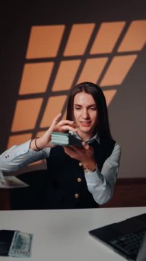 Genç bir kadın dizüstü bilgisayarın başında otururken para fırlatıyor. Bu kadın çok para kazandı. Finansal başarı kavramı. Dikey video 4k