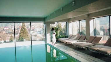 Genç bir kadın dağ manzaralı bir havuzda yüzüyor. Bir kadın kaplıcada dinlenmekten hoşlanır. Otel tatili konsepti 4k