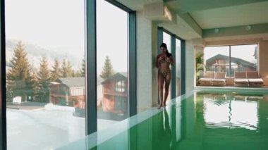 Genç bir kadın dağ manzaralı bir havuzda yüzüyor. Bir kadın kaplıcada dinlenmekten hoşlanır. Otel tatili konsepti 4k