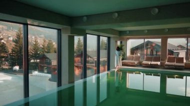 Genç bir kadın dağ manzaralı bir havuzda yüzüyor. Bir kadın kaplıcada dinlenmekten hoşlanır. Otel tatili konsepti 4k