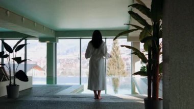 Genç bir kadın dağ manzaralı bir havuzda yüzüyor. Bir kadın kaplıcada dinlenmekten hoşlanır. Otel tatili konsepti 4k