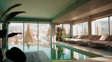 Genç bir kadın dağ manzaralı bir havuzda yüzüyor. Bir kadın kaplıcada dinlenmekten hoşlanır. Otel tatili konsepti 4k