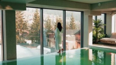 Genç bir kadın dağ manzaralı bir havuzda yüzüyor. Bir kadın kaplıcada dinlenmekten hoşlanır. Otel tatili konsepti 4k