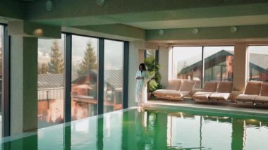 Genç bir kadın dağ manzaralı bir havuzda yüzüyor. Bir kadın kaplıcada dinlenmekten hoşlanır. Otel tatili konsepti 4k