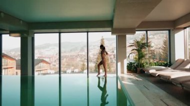 Genç bir kadın dağ manzaralı bir havuzda yüzüyor. Bir kadın kaplıcada dinlenmekten hoşlanır. Otel tatili konsepti 4k