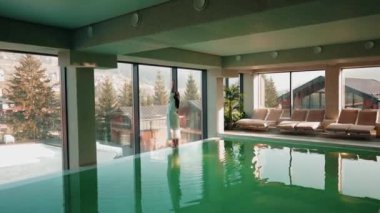 Genç bir kadın dağ manzaralı bir havuzda yüzüyor. Bir kadın kaplıcada dinlenmekten hoşlanır. Otel tatili konsepti 4k