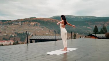 Spor yapan bir kadın bulutlu bir havada terasta dağların arka planında yoga yapıyor. Yoga ve meditasyon. Asanas. Manevi gelişim kavramı