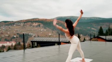 Spor yapan bir kadın bulutlu bir havada terasta dağların arka planında yoga yapıyor. Yoga ve meditasyon. Asanas. Manevi gelişim kavramı