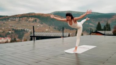 Spor yapan bir kadın bulutlu bir havada terasta dağların arka planında yoga yapıyor. Yoga ve meditasyon. Asanas. Manevi gelişim kavramı