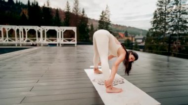 Spor yapan bir kadın bulutlu bir havada terasta dağların arka planında yoga yapıyor. Yoga ve meditasyon. Asanas. Manevi gelişim kavramı