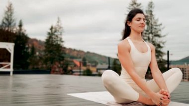 Spor yapan bir kadın bulutlu bir havada terasta dağların arka planında yoga yapıyor. Yoga ve meditasyon. Asanas. Manevi gelişim kavramı
