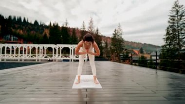 Spor yapan bir kadın bulutlu bir havada terasta dağların arka planında yoga yapıyor. Yoga ve meditasyon. Asanas. Manevi gelişim kavramı