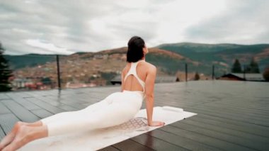 Spor yapan bir kadın bulutlu bir havada terasta dağların arka planında yoga yapıyor. Yoga ve meditasyon. Asanas. Manevi gelişim kavramı