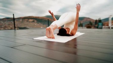 Spor yapan bir kadın bulutlu bir havada terasta dağların arka planında yoga yapıyor. Yoga ve meditasyon. Asanas. Manevi gelişim kavramı