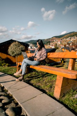 Genç bir kadın sonbaharda dağlarda tatilde bir dizüstü bilgisayarda çalışıyor. Kadın bir serbest çalışan doğada çalışır. Uzaktan çalışma konsepti. Tatilde çalışmak