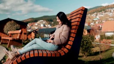 Genç bir kadın sonbahar dağlarında tatilde bir dizüstü bilgisayarın başında çalışıyor. Online iş. Uzak çalışma konsepti.