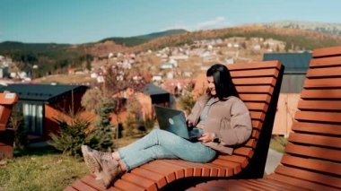 Genç bir kadın sonbahar dağlarında tatilde bir dizüstü bilgisayarın başında çalışıyor. Online iş. Uzak çalışma konsepti.