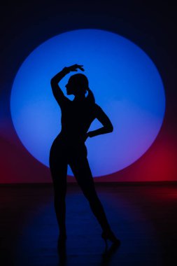 Mavi neon ışıkta dans eden bir kadının silueti. Mavi ışık çemberinde dans eden bir kadın. Dans ve hareket kavramı.