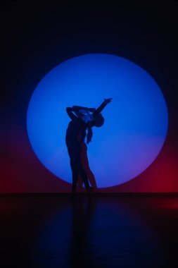 Mavi neon ışıkta dans eden bir kadının silueti. Mavi ışık çemberinde dans eden bir kadın. Dans ve hareket kavramı.