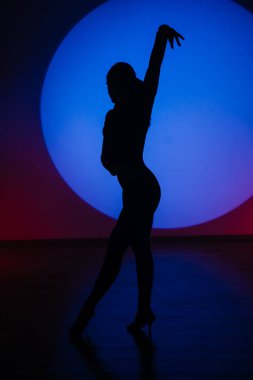 Mavi neon ışıkta dans eden bir kadının silueti. Mavi ışık çemberinde dans eden bir kadın. Dans ve hareket kavramı.